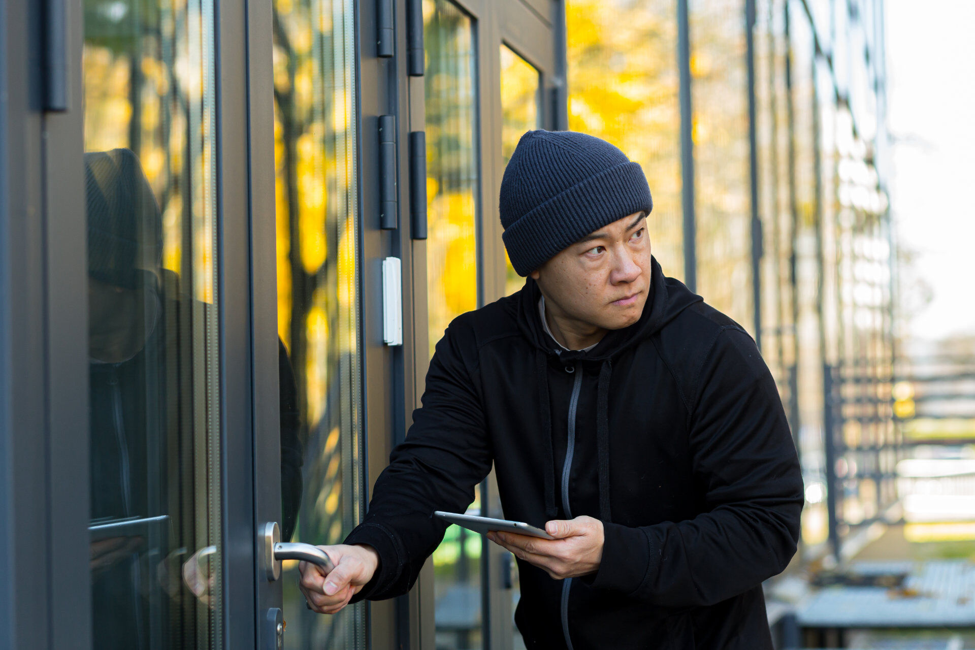 Male thief hacker tries to break the alarm in the house with a virus program, uses a tablet, Asian near the house