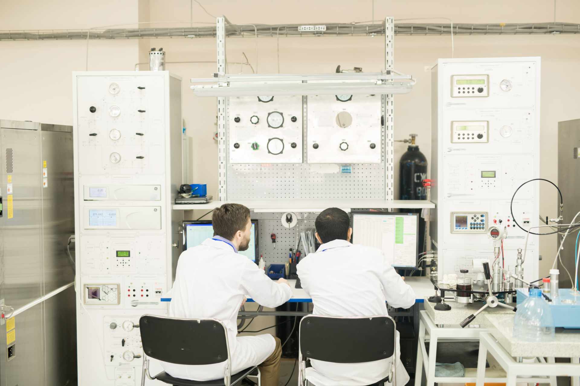 Rear view of concentrated male factory lab technician viewing information on computer connected to control cabinet while working in modern manometer plant